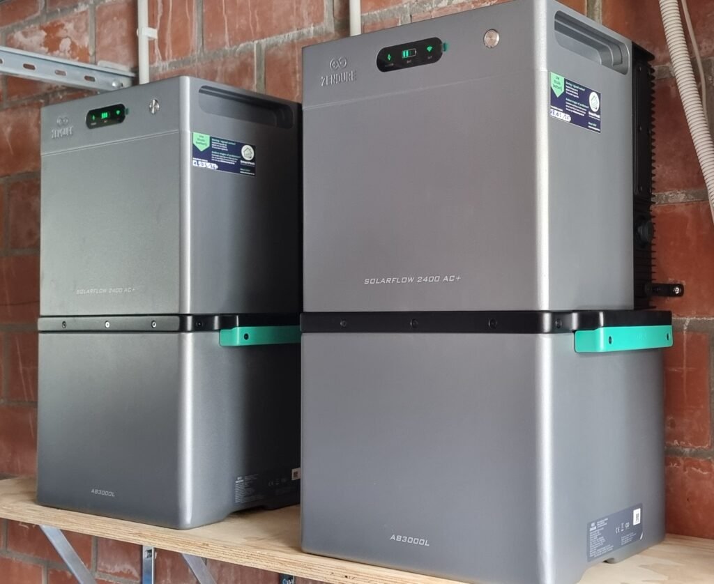 Two large gray solar inverters mounted on a wooden shelf against a brick wall, labeled SolarFlow 2400 AC+ and AB3000L.